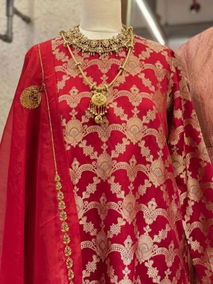 A close-up of the red Banarasi kurta, highlighting the intricate gold weaving and the stunning traditional necklace it's paired with.
