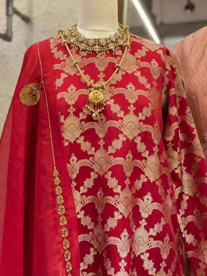A close-up of the red Banarasi suit, showcasing the intricate gold weaving and the stunning layered necklace that completes this regal ensemble.