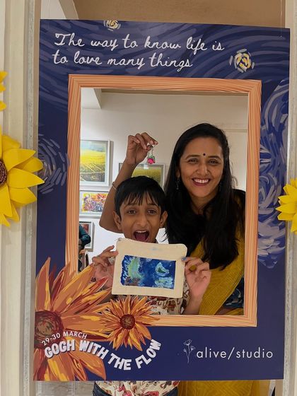 A mother and son duo having a blast at our "Gogh with the Flow" event, posing with their artwork in our themed photo frame.