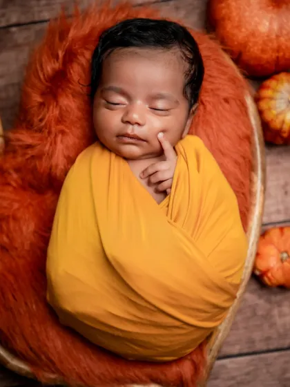 A little bundle of sunshine. This close-up shot captures the peaceful sleep of a baby wrapped in a warm, golden-yellow swaddle.