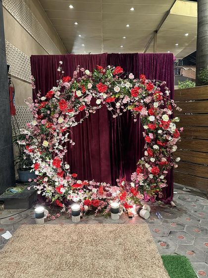 This circular floral arch against a rich velvet curtain serves as a beautiful and unique photo point for guests. The combination of red, pink, and white flowers creates a romantic and eye-catching installation.