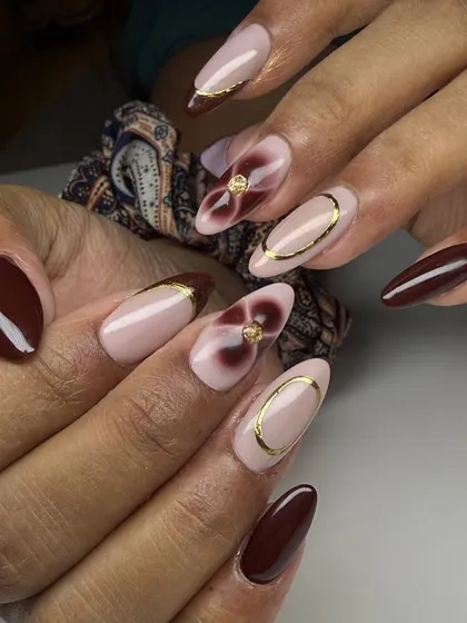 A sophisticated and artistic nail set. This design features a mix of solid brown nails and nude accent nails with abstract floral patterns and delicate gold ring details.