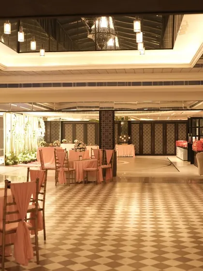 A wide view of the indoor hall, showing the elegant checkered flooring and the pink-themed seating arrangement. The space is ready to welcome guests for the post-ceremony celebrations.