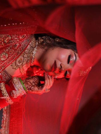 An artistic shot of a bride lying under her red veil. This angle beautifully showcases her dramatic eye makeup and bold red lip.