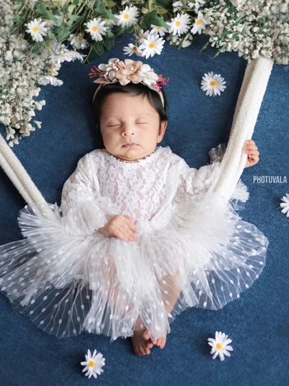 Dreaming among the daisies. This sweet newborn rests peacefully in a swing adorned with delicate white flowers.