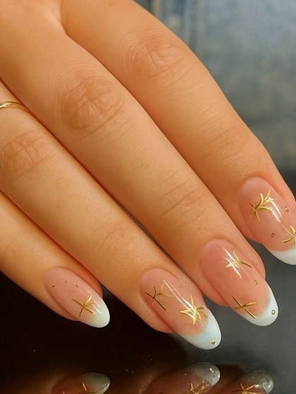 A closer look at a modern French manicure, featuring delicate gold star embellishments and tiny rhinestones for a touch of sparkle.