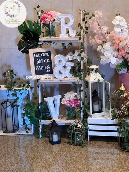 A charming "Welcome Home Babies" setup. This rustic-chic corner features a decorative ladder, lanterns, and floral arrangements to celebrate the arrival of new family members.
