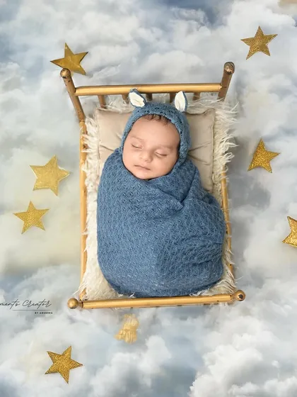 Dreaming among the stars. This newborn, wearing a cute bunny-eared cap, is nestled in a tiny bed that seems to float on a cloud-filled, starry sky.