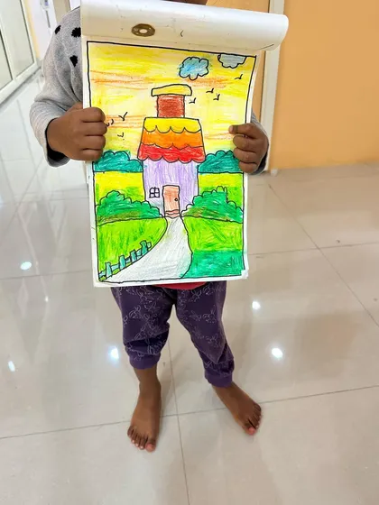 A student proudly holding up their colourful house drawing. Learning to draw landscapes and buildings is a great way to understand perspective and composition.