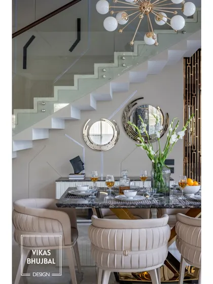 In this duplex home in Gujarat, the dining area is set against a modern staircase with a glass railing. The design uses sculptural chairs and a statement chandelier to create an elegant dining experience.