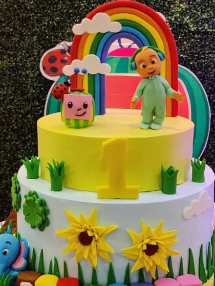 A bright and cheerful two-tiered Cocomelon cake, decorated with a rainbow, sunflowers, and the iconic characters.