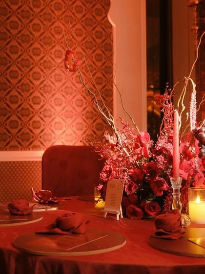 A round dining table with a dramatic red floral centerpiece, bathed in the warm, monochromatic light of the room.