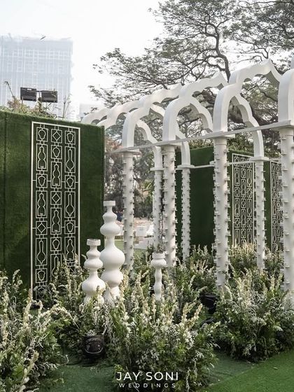 A side view of the striking all-white archway, highlighting the intricate pillar details and the lush greenery that lines the path, creating a beautiful contrast and a sense of depth.
