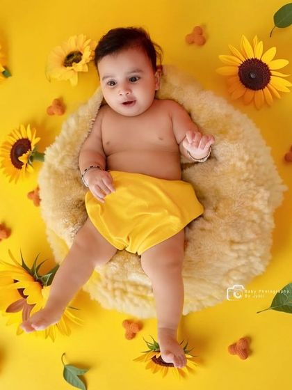 A bright and cheerful studio shot with a vibrant yellow theme. The baby is lying on a soft cushion surrounded by sunflowers, creating a sunny and happy portrait.