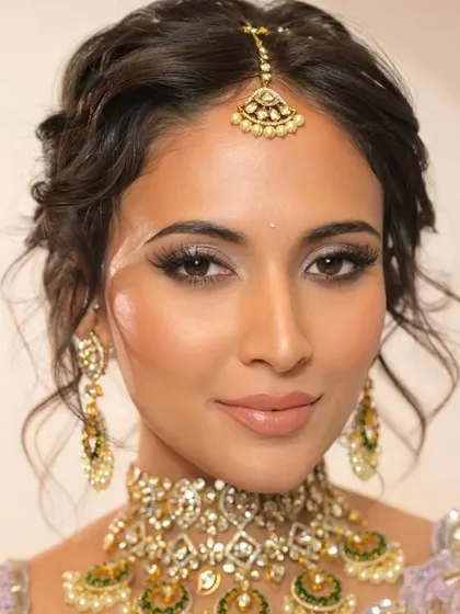 A close-up on a trendy tousled updo. This style has soft, face-framing tendrils and a textured finish, making it a perfect choice for a modern bride wearing a pastel lehenga.