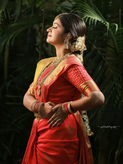 A side profile shot capturing the bride in a moment of tranquility. The natural light highlights her features and the texture of her red saree.