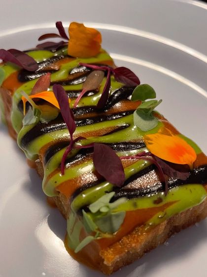 A close-up of the savory toast canapé, showing the intricate sauce work and the fresh, vibrant garnishes.
