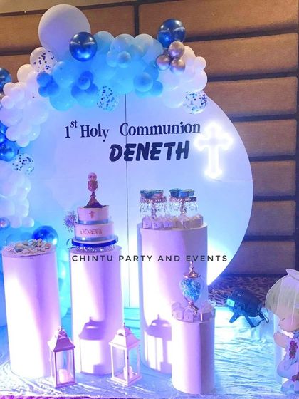 A First Holy Communion decoration for a boy with an angel theme. The setup uses blue and white chrome balloons and illuminated pedestals.