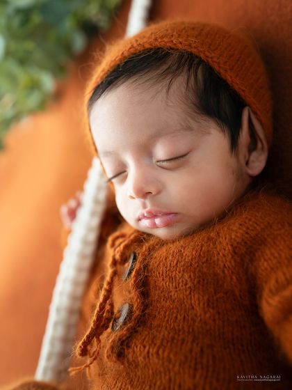 A close-up of a two-week-old newborn's face, highlighting their peaceful expression and the soft texture of the knit bonnet.