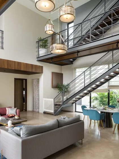 This double-height living and dining area is unified by a dramatic metal staircase and bridge. We used pops of color in the furniture and a vibrant abstract rug to bring energy and personality to the industrial-chic space.