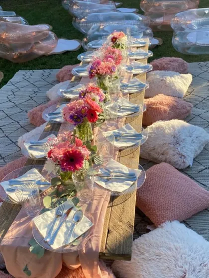 A unique picnic setup with inflatable clear chairs and fluffy pink and white cushions. This modern and playful take on a picnic is perfect for a fun and stylish event.