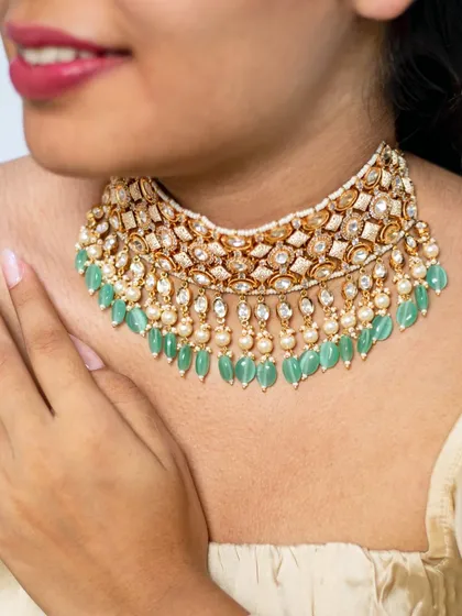 This kundan choker features a classic design with pearl and mint-green bead droppings. It's a versatile piece that can be worn by brides, bridesmaids, or guests for a touch of timeless elegance.