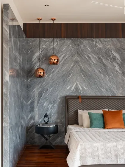 In the second master bedroom, a wall of book-matched grey marble creates a dramatic and luxurious backdrop. Copper pendant lights add a warm metallic accent, complementing the rich tones of the timber floor.