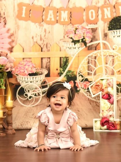 Crawling into her first birthday with a huge smile. This shabby-chic setup with pink florals and a vintage-style bicycle creates a dreamy, romantic scene for her special day.