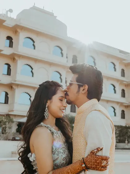 A tender moment with the groom kissing the bride's forehead, backlit by the morning sun in Udaipur.