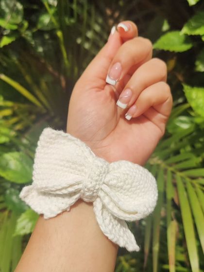 A close-up of the white crochet bow, highlighting the detailed stitch work. It's made with a high-quality elastic to be both beautiful and durable.