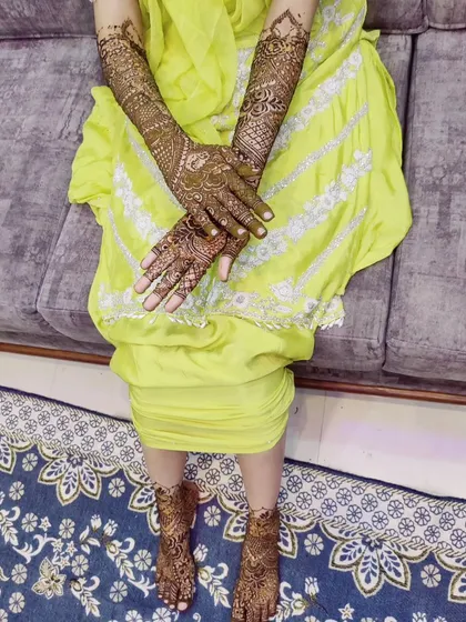 A beautiful bride showing her full mehndi work. The designs extend up the arms and include delicate patterns on the feet for a complete and traditional look.