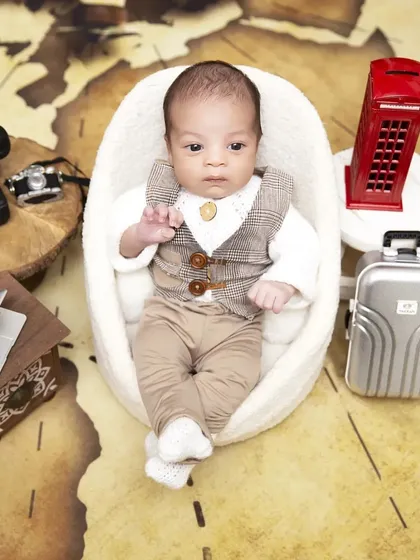 A different perspective of the "Boss Baby" travel theme, showing the full setup with a world map backdrop. The awake baby is posed in a comfortable chair, surrounded by travel-related props.