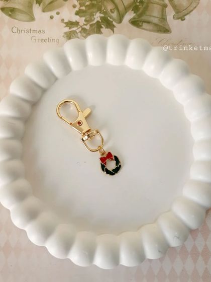 A Christmas wreath charm keychain with a little red bow. It's a classic and elegant festive accessory.