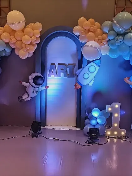 An out-of-this-world space theme for a first birthday. This setup features an astronaut, a rocket ship, planets, and a galaxy of balloons in shades of blue and orange, creating an adventure for a little explorer.
