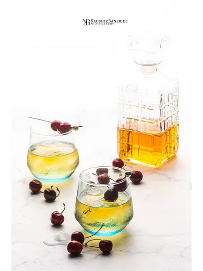 A light and airy shot of a whiskey cocktail, garnished with fresh cherries. This high-key style offers a fresh, clean alternative to traditional dark liquor photography, perfect for summer menus.