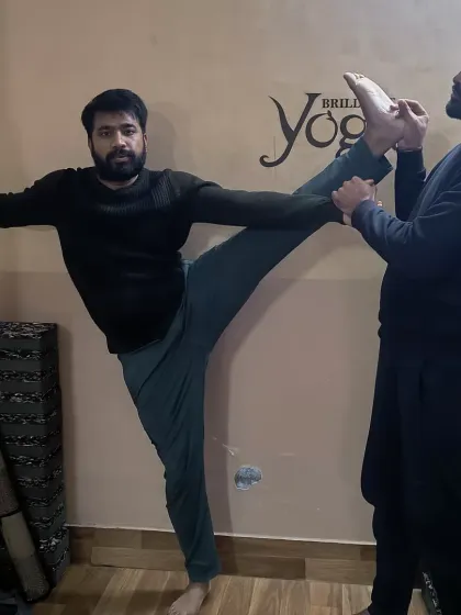 An instructor assists a student in a standing leg extension, helping him safely increase his range of motion. Personalized adjustments are key to preventing injury and making progress.