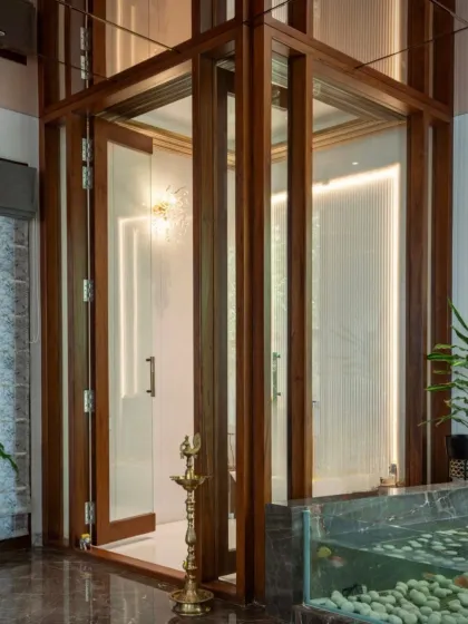 A close-up of a glass-enclosed pooja room, framed in rich wood. The design creates a sacred, light-filled space that is visually connected to the home while remaining distinct.
