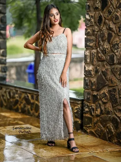 A confident pose in a striking silver outfit, with the model's hand on her hip, showcasing the dress's texture and side slit.