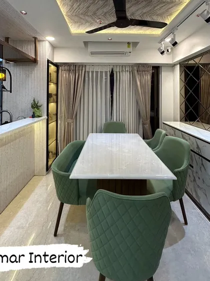 A beautiful dining room with quilted green chairs and a white marble table. The design features a textured wooden false ceiling and a mix of industrial and modern lighting.