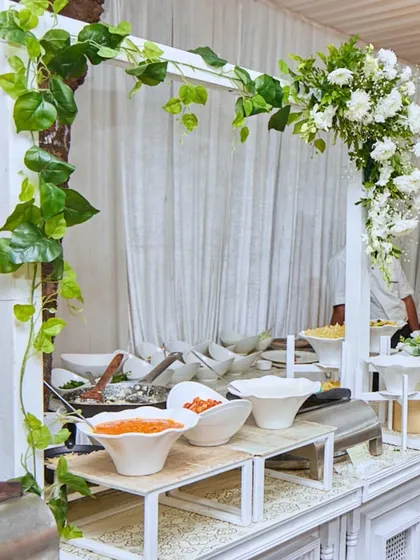 A clean and elegant white buffet station, adorned with fresh greenery. This minimalist setup is perfect for a sophisticated event where the food is the star.