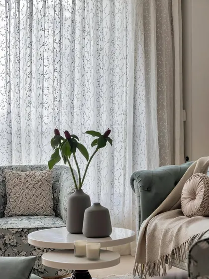 Soft textures and patterns create an inviting atmosphere. Here, a floral armchair and a classic sofa are layered with throws and pillows against a backdrop of sheer, patterned curtains.