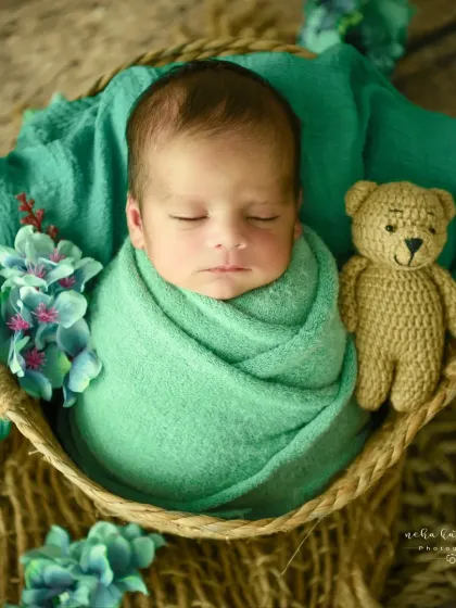 A simple and sweet portrait. This baby is swaddled in green, with just one teddy bear companion, keeping the focus on their serene expression.