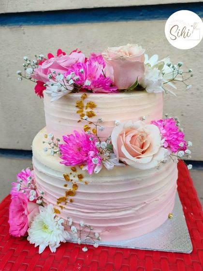 Pretty in pink for a beautiful engagement party. This two-tier cake features a soft pink ombre texture, accented with fresh pink and white flowers and a sprinkle of gold leaf for a touch of sparkle.