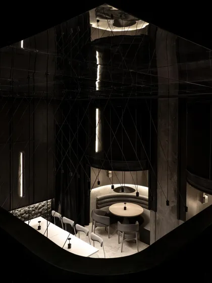 A view from above, looking down into the dining area. The geometric arrangement of tables is softened by the curved booths, and the entire scene is captured in the mirrored ceiling.