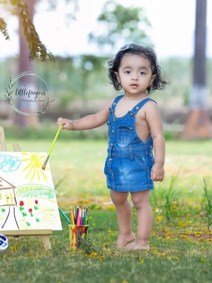 This little one is proudly showing off her masterpiece. The 'Little Artist' theme is a wonderful way to capture your child's creative side in a natural, outdoor setting.