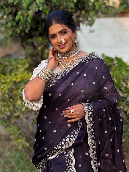 A beautiful portrait of a bride in a dark purple saree. The makeup features a soft glow, a traditional Maharashtrian nath, and layered silver-toned jewellery for a modern yet classic feel.