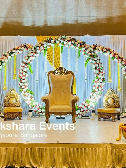 A unique engagement stage with two large floral rings as the backdrop. The design is simple yet striking, with traditional chairs and marigold bowls adding a classic touch.