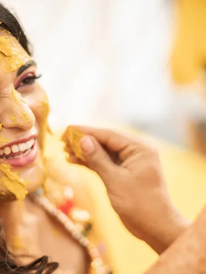 A close-up of the bride's joyful, laughing face as she gets haldi applied.