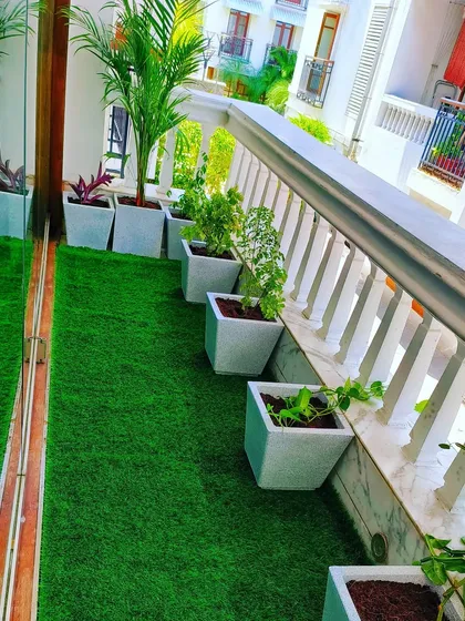 This elegant balcony design uses a row of uniform white planters against a glass railing, creating a clean, sophisticated look. The lush artificial grass provides a soft surface and year-round greenery without any watering or mowing.