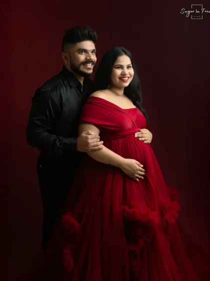 A joyful and elegant couple's portrait. Their bright smiles add a touch of warmth to the dramatic red backdrop and formal attire.